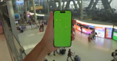 Modern pazarlama potansiyeli sunan canlı havaalanı aktivitelerini gösteren yeşil ekranlı akıllı telefon. Yeşil ekran ürün yerleştirme veya seyahat reklamları için mükemmel marka olanaklarını artırır.