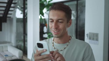 Akıllı telefonu elinde tutan adam sosyal medyadaki arkadaşlarıyla canlı bir şekilde çevrimiçi iletişimde gülümsüyor. Beyaz erkek telefonda yazarken arkadaşlarıyla konuşmaktan zevk alıyor.