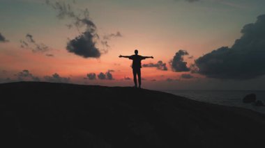 Siluet adam dağın tepesinde beliriyor. Kızıl günbatımına karşı. Güneş batımında heybetli bir figür.