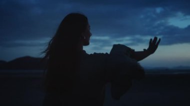 Doğada iç huzuru bulan bir kadın. Genç bir kadının silueti dağlarla birlikte güzel doğal bir manzarada duruyor, kollarını açıyor ve dramatik alacakaranlık ışıklarının ve rüzgarın saçlarını savuruşunun tadını çıkarıyor.