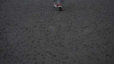 Kırmızı ve beyaz spor ayakkabılarla asfalt yolda yürüyen birinin alçak açılı görüntüsü. Deniz kenarında huzurlu bir akşam yürüyüşü hareketin ruhunu yakalıyor ve şehir manzaralarında kişisel yolculuğun heyecanını yakalıyor.
