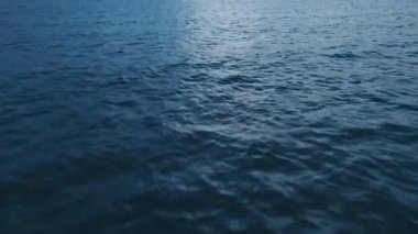 Solan gökyüzünün altında mavi deniz dokusu. Koyu mavi dalgalı su yüzeyi dengesiz ve gizemli bir atmosfer yaratıyor. Arka plan ve doğa, deniz manzaraları veya sükunetle ilgili projeler için mükemmel.