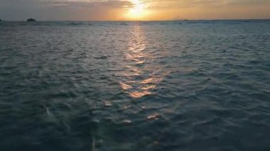 Altın gün batımı, sakin okyanus sularına yansıyarak büyüleyici bir ışık yolu yaratıyor. Uzak adalar, sakin manzaraya huzur katıyor. Okyanus ışıldıyor altın sabah ışığında