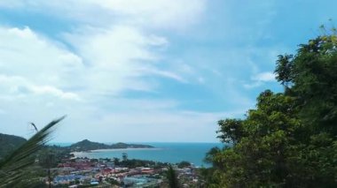 Bereketli palmiye ağaçları, tropik adanın ve engin okyanusun nefes kesici manzarasını, tüylü beyaz bulutlarla kaplı parlak mavi gökyüzünü, huzurlu ve huzurlu manzarayı oluşturur. Palmiye yapraklarıyla çerçevelenmiş okyanus ufku