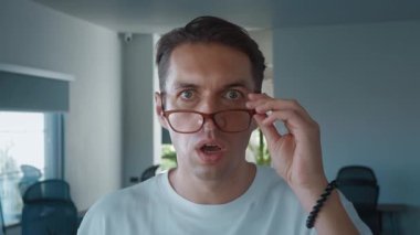 Surprised man lowering glasses in disbelief while working from home, showcasing shock and amazement in his home office, capturing moment of unexpected reaction and emotion. Surprise in man