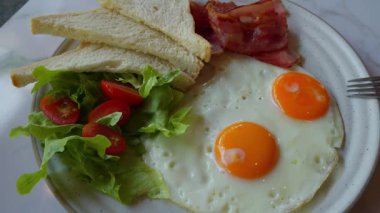 Tam ve sağlıklı bir kahvaltı. İki mükemmel kızarmış yumurta, yanında çıtır pastırma şeritleri, altın kahverengi tost ve taze salata ile birlikte vişneli domates ve marul ile birlikte kahvaltı tabağının orta parçasıdır.