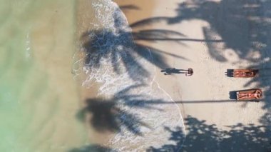 Kristal berrak turkuaz su, turistlerin palmiye ağaçlarının altındaki güneşli yataklarda dinlenerek huzurlu ve huzurlu bir tatil sahnesi yarattıkları sahili nazikçe yıkıyor. Palmiye gölgeleri lüks sahil kaçışının üzerine uzanıyor