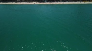 İHA görüntüsü. Güzel zümrüt yeşili okyanus suyunun, turistlerle beyaz kumsalda buluşup yaz tatilinin tadını çıkardığı, hareketli ve dingin tropikal tatil şehveti yaratan hava manzarası.