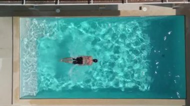 Vücudunu tazele, görüşünü yükselt. Yukarıdan bakıldığında, erkek turistler güneşli yaz günlerinde otelin yüzme havuzunun turkuaz suyunda huzur içinde yüzerek tatilinin tadını çıkarıyorlar. Drone görünümü