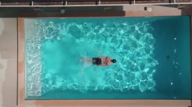 Hava manzarası, berrak mavi suyla dolu lüks yüzme havuzunda yüzen ve dinlenen turistleri yakalıyor, güneşli yaz gününün sıcaklığının tadını çıkarıyor. Stresi mükemmel bir simetride yüzdür