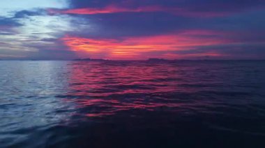 Suya yansıyan altın bulutlar. Gün batımının canlı renkleri gökyüzünü boyarken ve sakin okyanus sularını yansıtırken uzak adalarla güçlendirilmiş büyüleyici bir sükunet manzarası yaratır. Adadaki gece hayatı