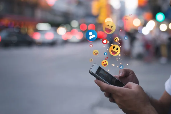 Genç adam akıllı telefonuyla emoji yolluyor. Bir cep telefonu kullanarak duygu simgesi metin iletisi.
