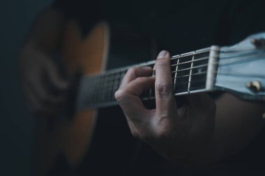 Akustik gitar çalan genç bir adamın ellerinin yakın çekimi.