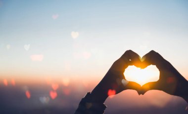 Female hands in the shape of a heart on an abstract tropical sunrise background with haert bokeh, sun light flares, waves, and blur. Copy space of joyful, freedom-loving travel concept. clipart