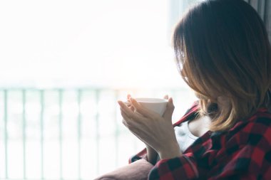 A young woman relaxes on her bed while drinking coffee in her morning bedroom.
