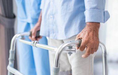 senior man patient receives physical therapy. Attractive professional caregiver women assist and encourage older, more experienced men as they practice walking slowly with a walker in nursing homes.