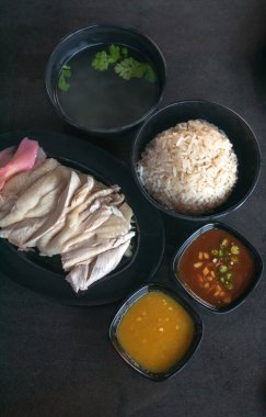 Çorba ve ahşap masa dokusunda iki soslu Hainanese tavuğu pilavı.