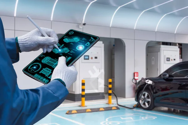 Genç bir tamirci, aracın motoruna çömelmiş vaziyette duran tablet cihazına bakıyor ve teknik denetim yapıyor.
