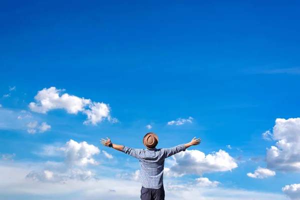 Young man\'s rising hands in a copy space against an abstract blue sky and white cloud background. Concept of adventure travel and freedom.