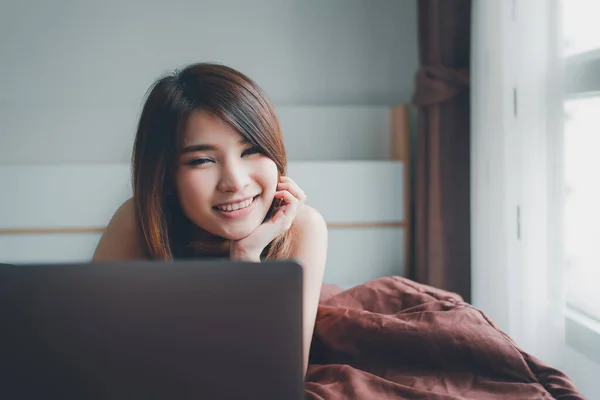 stock image a young Asian woman with a smile reading on her laptop while resting down on the bed. working from home while under quarantine. Social estrangement Personal Isolation