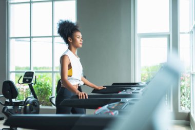 Bir kadın koşu bandında koşarken panoramik bir pencerede egzersiz yapıyor ve sağlıklı bir yaşam tarzı sürüyor..