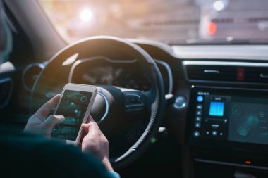 Genç adam akıllı telefonuna odaklanmış bir şekilde otomobil kullanıyor. Yakışıklı, yeni bir evcar içindeki genç adam dokunmatik ekranı kontrol ediyor.