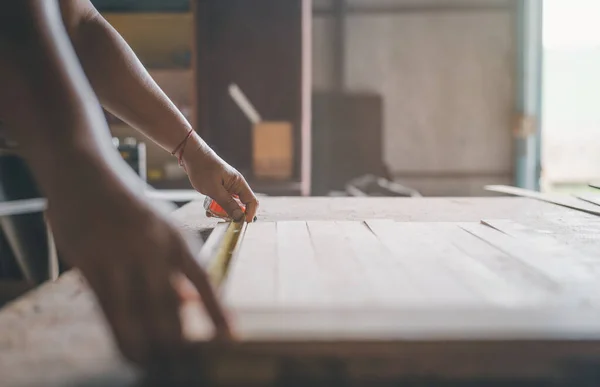 stock image Unidentified craftsman's hands marking a piece of wood in the vice of a workbench with a measuring tape and a pencil