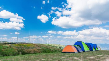 Güzel rüzgar jeneratörleri ve çayırın ortasına kurulmuş bir çadır..