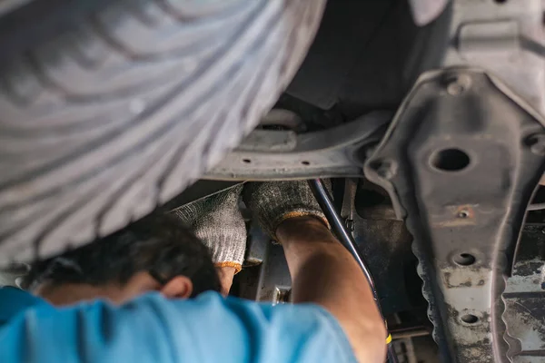 Using a socket wrench, the auto mechanic performs suspension maintenance in the garage, replaces a spare part, and verifies the vehicle's mileage, checking and maintenance service concept.
