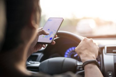 Bir şehirde araç kullanırken akıllı telefon kullanan bir adam, gün batımında mobil bir cihazın GPS navigasyon sistemini kullanıyor