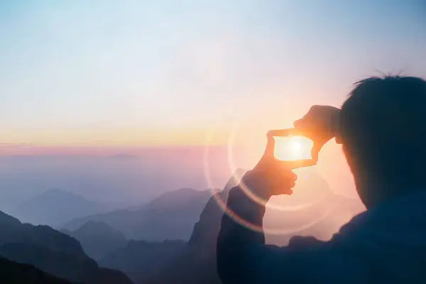 Silhouette of a person capturing sunlight in their hand during a beautiful mountain sunrise, creating a magical effect