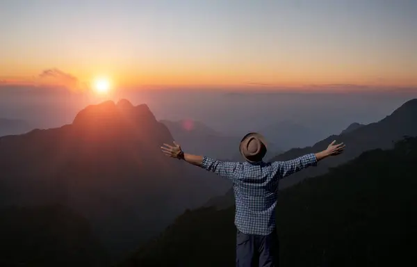 A solitary man with open arms welcomes the sunrise atop a serene mountain peak, embracing the new day's promise