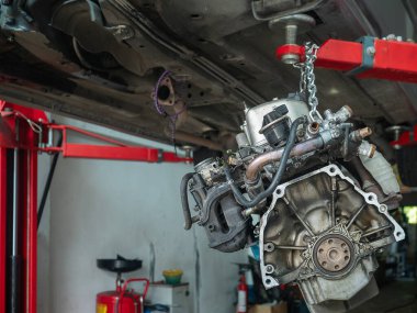 Otomotiv tamiri veya bakım işlemi sırasında araba motoru bir garajdaki zincir tarafından askıya alınır.