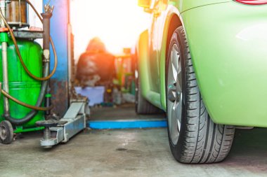 Yakından bir benzin istasyonunda yakıt dolu yeşil bir arabanın görüntüsü, lastiği ve pompayı vurguluyor.