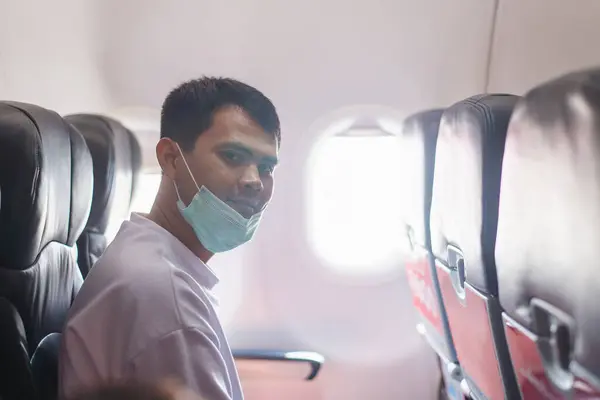 A young man dons a protective face mask while seated inside an airplane, illustrating safe travel practices