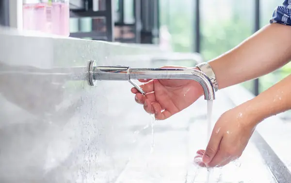 stock image Close-up of hands washing under a modern faucet in a bright kitchen, emphasizing cleanliness and hygiene.