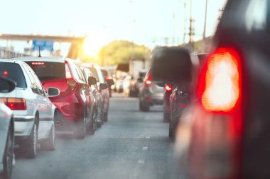 Gün batımında bir şehir caddesinde trafiğe takılan araçlar, kentsel trafiği ve günlük trafik sorunlarını vurguluyor.