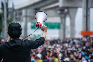 Elinde megafon tutan bir kişi, eylemcilik, liderlik ve halka açık gösterileri sembolize eden bir protesto sırasında büyük bir kalabalığa hitap ediyor..