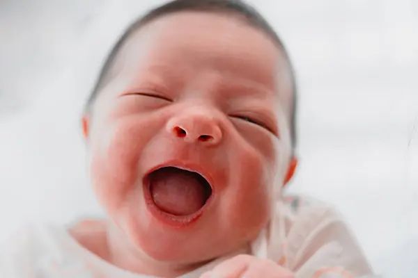 Stock image Close-up portrait of a joyful newborn baby with eyes closed, laughing heartily, capturing pure happiness and innocence.