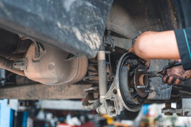 Bir araba fren sistemi üzerinde çalışan bir tamirci, bir oto tamir atölyesinde arka tekerlek bileşenlerine odaklanıyor..