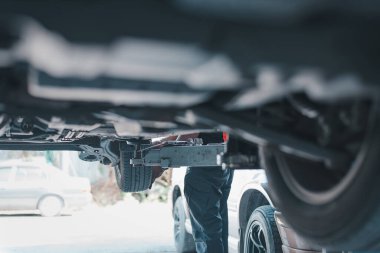 Bakım ve onarım için kaldırılırken arabanın şasisini inceleyen bir tamircinin yakın görüntüsü.