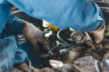 Otomotiv parçalarıyla çevrili bir otomotiv motoru üzerinde titizlikle çalışan bir tamircinin elleri yakın plan çekilmiş..