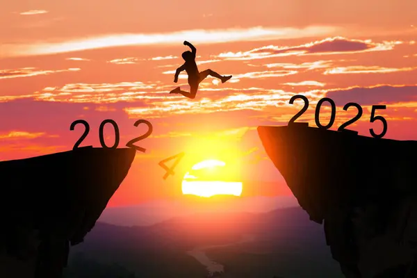 2024 uçurumundan gün batımında 2025 uçurumuna atlayan bir insanın silueti, yeni yıl geçişini simgeliyor..