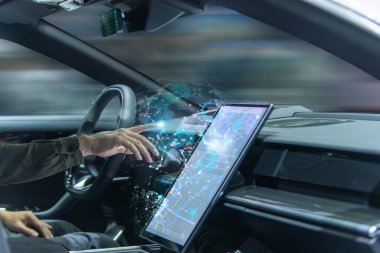 Sürücü, modern bir elektrikli aracın içinde ileri teknoloji ve yenilik içeren yüksek teknolojili dijital dokunmatik ekran arayüzü ile etkileşime geçiyor..