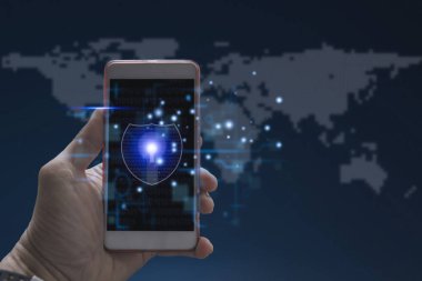 Küresel dijital ağın ortasındaki siber güvenliği sembolize eden anahtar deliğiyle parlayan bir kalkanı gösteren akıllı telefonu tutan bir el..