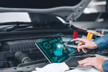 Bir tamirci, bir atölyede açık kaputun altındaki elektrikli araç motorunu analiz etmek için bir dizüstü bilgisayar üzerinde gelişmiş tanı yazılımı kullanır..