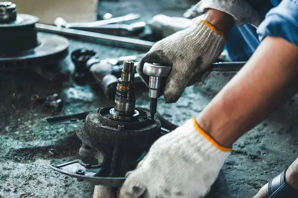 Endüstriyel atölyedeki yağlı makine parçalarını tamir etmek için bir elektrikli alet kullanan tamircinin ellerinin yakın çekimi.