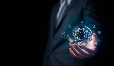 Takım elbiseli bir işadamı, küresel bağlantıyı, teknolojiyi ve iş dünyasındaki yeniliği sembolize eden parıldayan bir dijital dünya hologramı sunuyor..