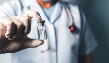 Eldiven ve üniforma giyen, içinde aşı ya da ilaç bulunan temiz bir ilaç şişesi taşıyan bir sağlık görevlisinin yakın çekimi..