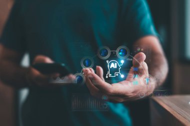 Veri grafikleri, yenilikler ve teknoloji simgeleri ile gelecekteki yapay zeka arayüzünü görselleştirirken akıllı telefon kullanan bir kişi.